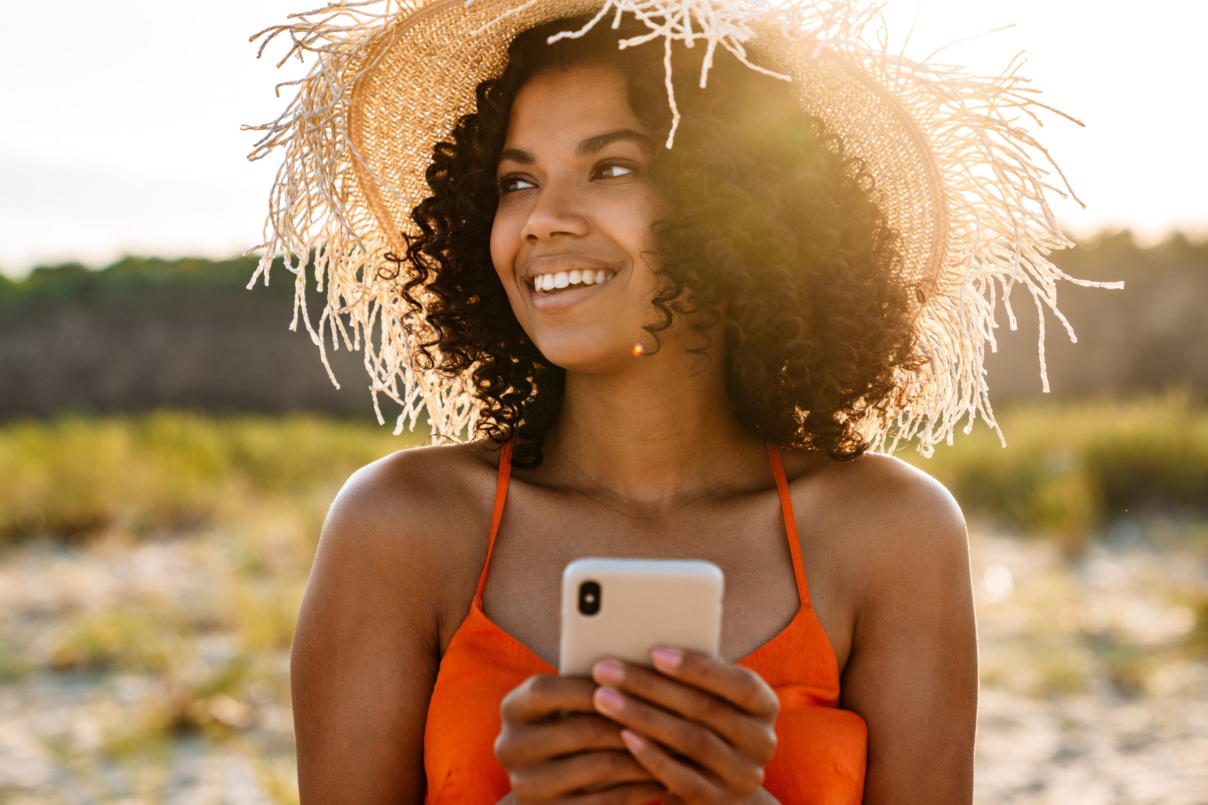 female with a hat holding cell phone, smiling